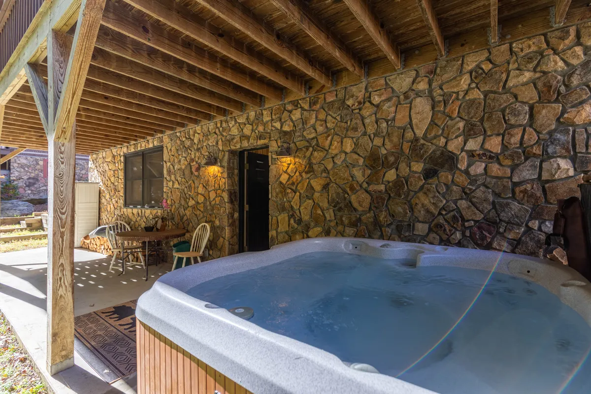 A cozy indoor scene featuring a bubbling hot tub set against a stone wall, with wooden beams overhead and a dining table nearby. This space suggests opportunities for relaxation and socializing after a day of group activities.