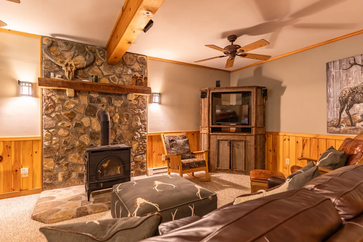 A warm, rustic living room featuring a stone fireplace, exposed wooden beams, and comfortable seating. The decor evokes a cozy, mountain-lodge atmosphere, ideal for gathering after a day of outdoor exploration.