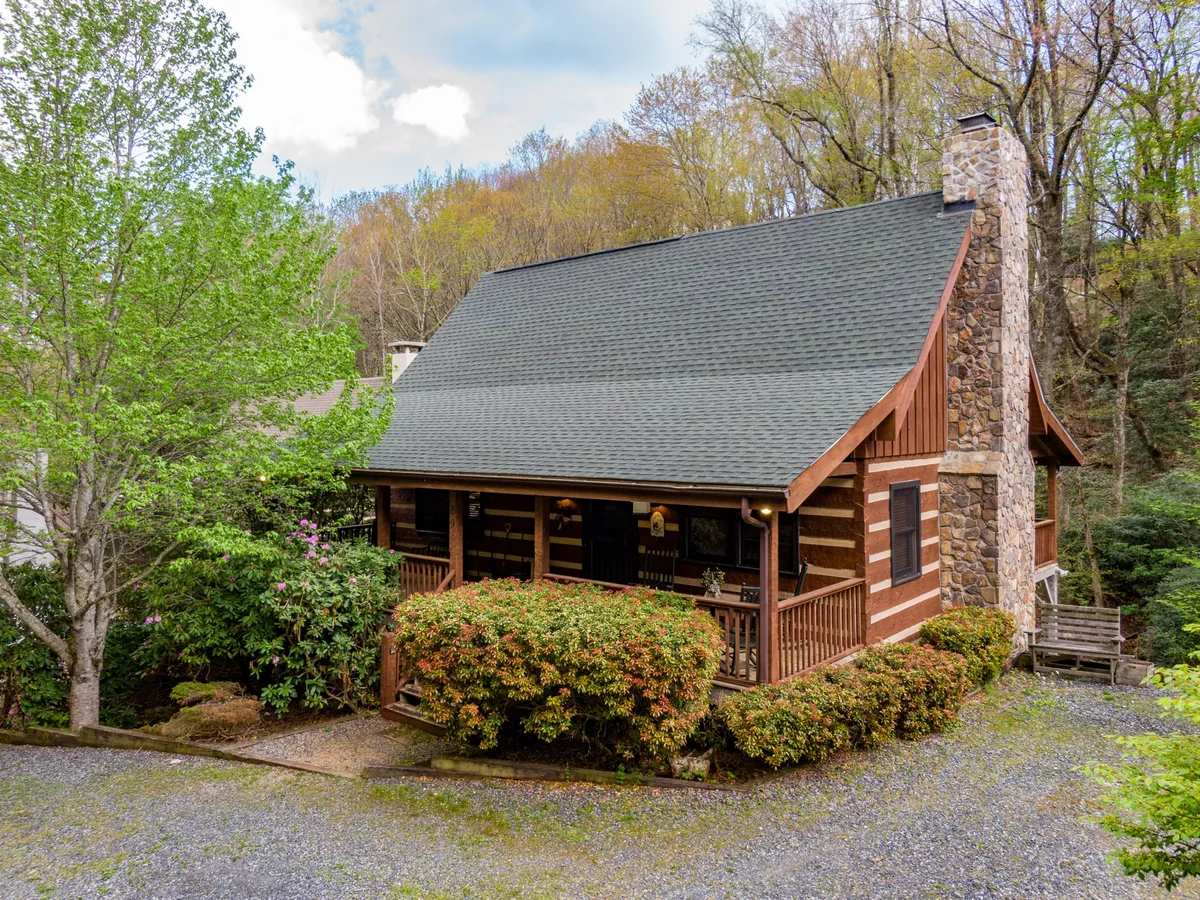This image beautifully captures the log cabin's exterior, complete with a stone chimney, spacious front porch, and lush green surroundings. The scene evokes a sense of retreat and connection with nature, inviting families to relax outside or set off on nearby adventures.