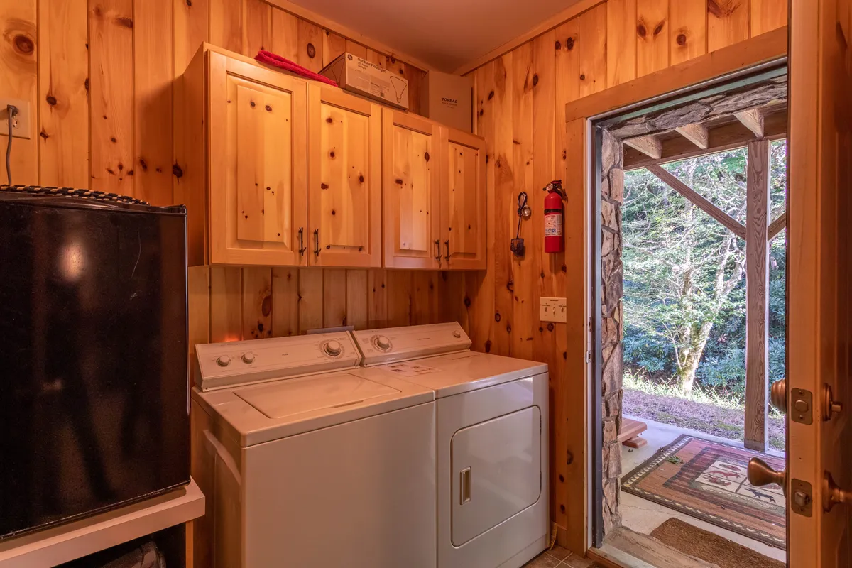 A view of the laundry area with a washing machine, wooden cabinets, and a doorway leading outside. The scene highlights practical amenities and a glimpse of the outdoors.