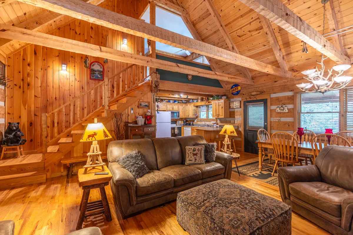 An open-concept living and dining area with wooden beams, plush sofas, a welcoming dining table, and a staircase, all bathed in warm natural light. The space is perfect for family gatherings and intimate celebrations after a day spent exploring the outdoors.