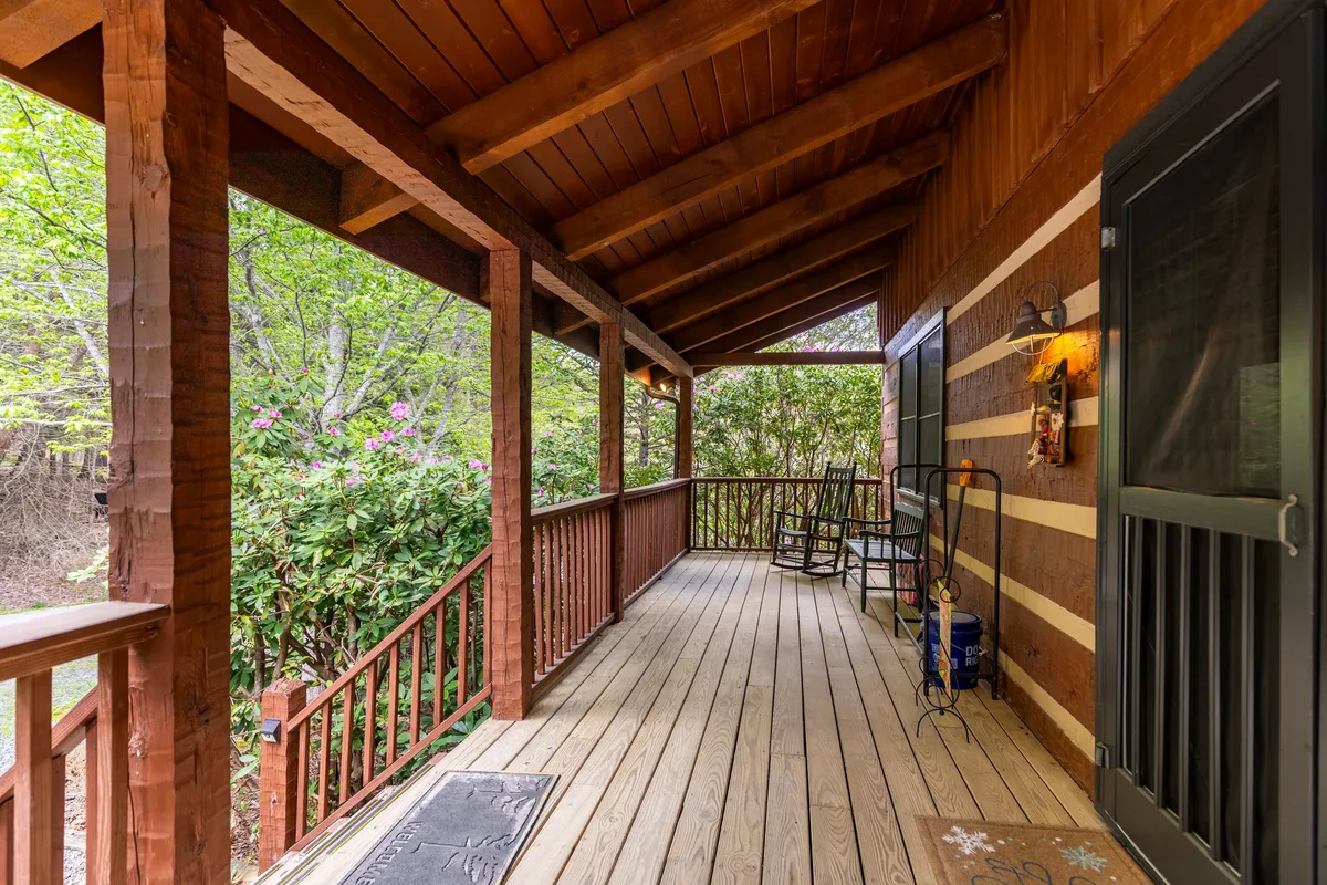 A classic wooden rocking chair sits on a welcoming front porch, surrounded by lush greenery. The scene suggests a peaceful spot to unwind, read a book, or connect with family after a day of adventure.
