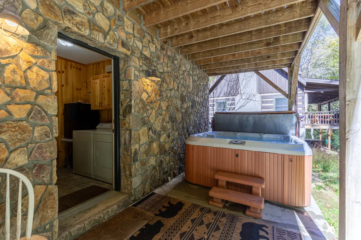 A tranquil patio scene showing a hot tub nestled against a stone wall near a doorway, with subtle greenery in the background. The area feels peaceful and private, capturing the appeal of soaking surrounded by nature and mountain air.
