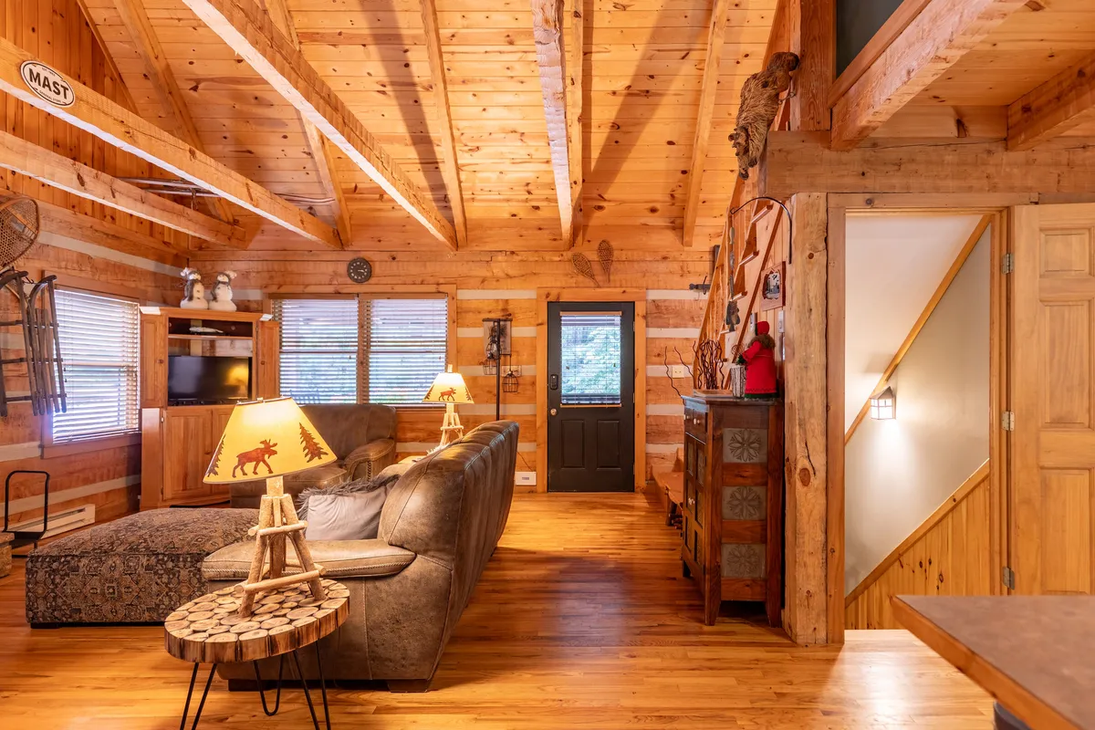 A welcoming living space with a plush sofa, distinctive wooden beams, and a lamp featuring a forest motif. The wooden furniture and soft lighting create a serene, nature-inspired environment, perfect for unwinding or enjoying quiet moments as a couple.