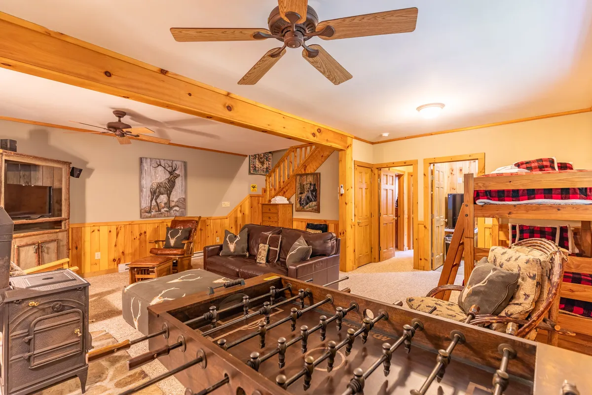 A lower-level den featuring twin bunk beds built into the wooden walls, a foosball table at center, and comfortable seating. The room exudes a playful and relaxed vibe, ideal for family fun and late-night activities.