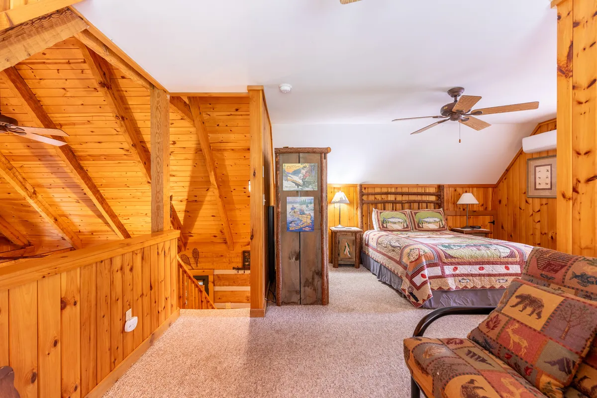 A loft area with a comfortable bed and a sofa under exposed wooden beams, accented by decorative artwork. The setting is intimate yet open, ideal for extra guests or teens seeking a cozy, semi-private nest.